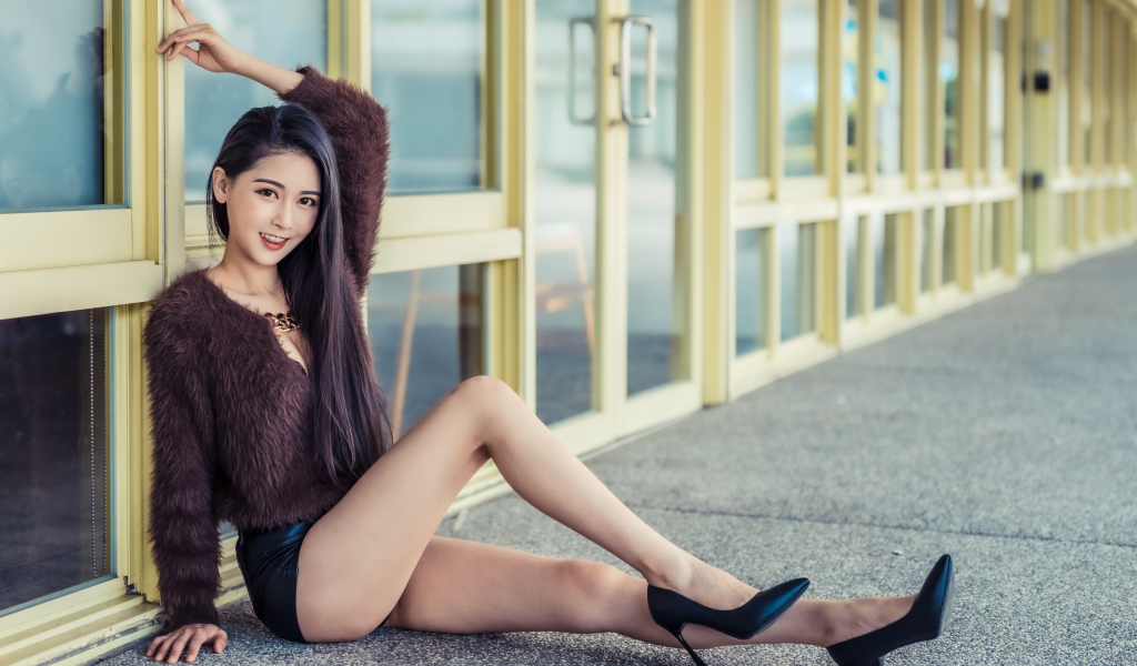 Девушка в свитере сидит у стеклянной стены 