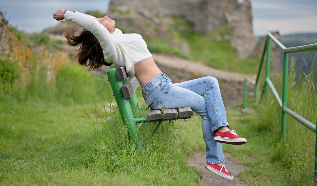 Девушка в синих джинсах сидит на лавке 