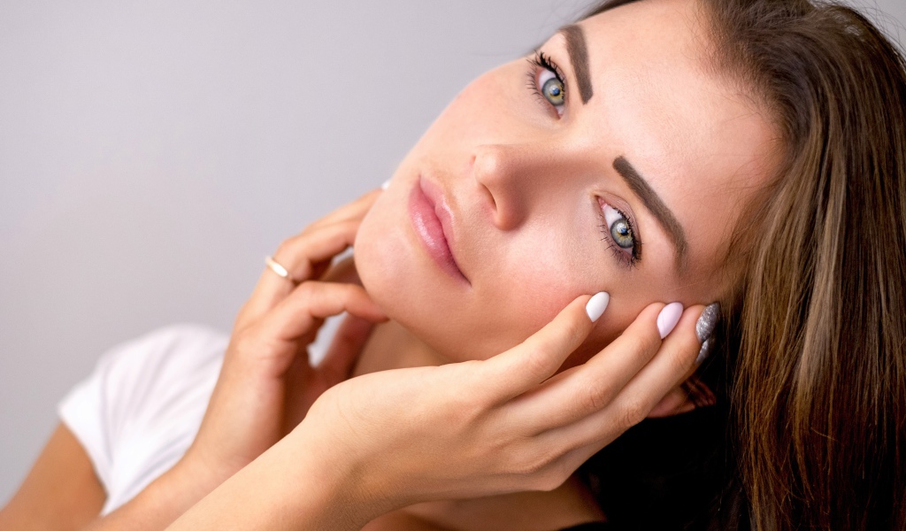 Девушка с руками у лица на сером фоне