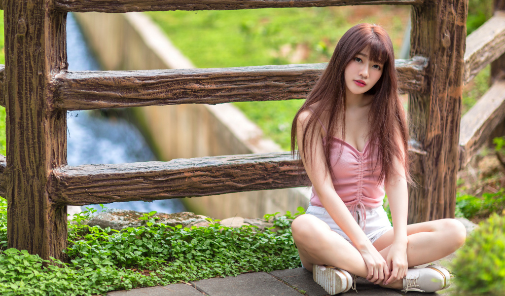 Длинноволосая азиатка сидит у забора 