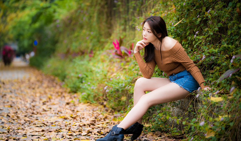 Задумчивая азиатка сидит в парке осенью 