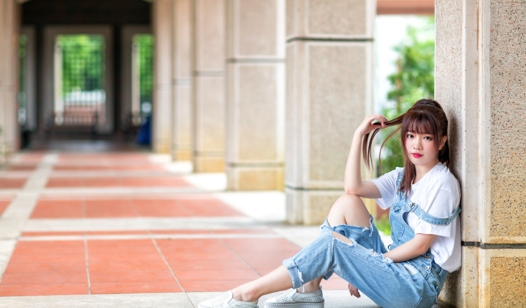 Грустная девушка азиатка сидит у колонны