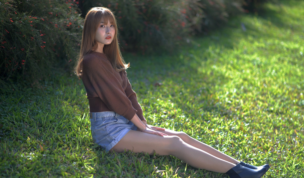 Грустная девушка азиатка сидит на зеленой траве 