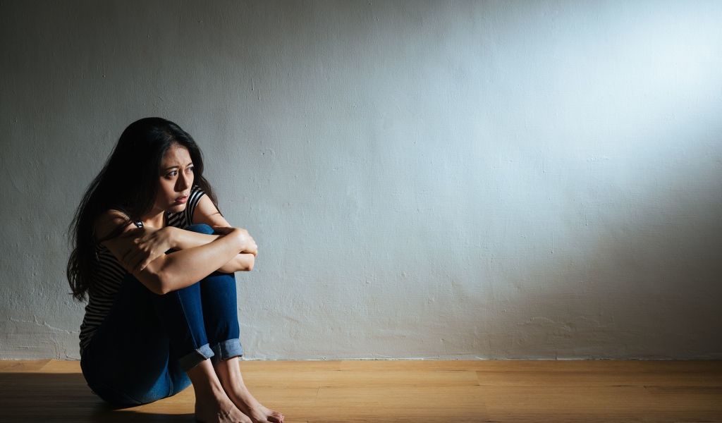 Испуганная девушка азиатка сидит у стены