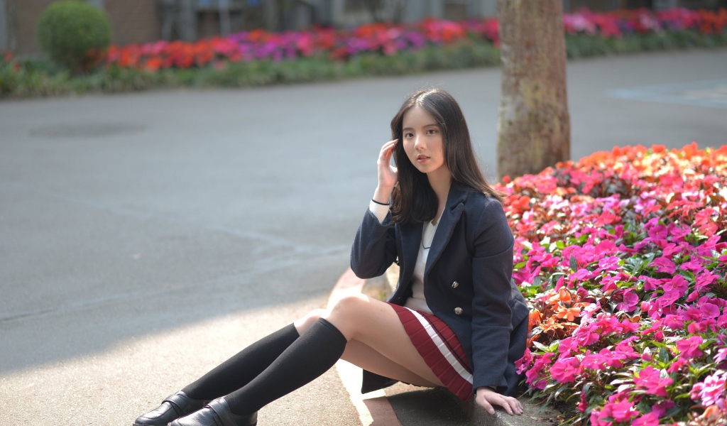 Девушка школьница сидит на земле у клумбы 