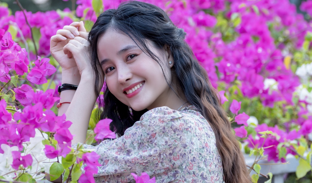 Улыбающаяся девушка азиатка на фоне розовых цветов
