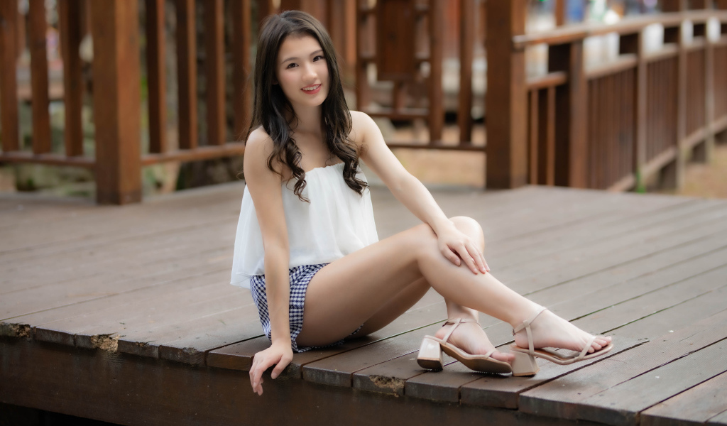 Улыбающаяся девушка азиатка сидит на мосту 