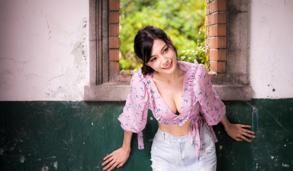 Улыбающаяся девушка азиатка стоит у окна 