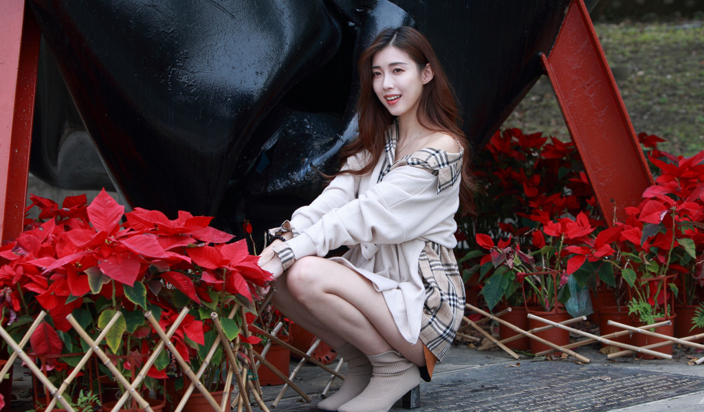 Улыбающаяся азиатка сидит у красных цветов 