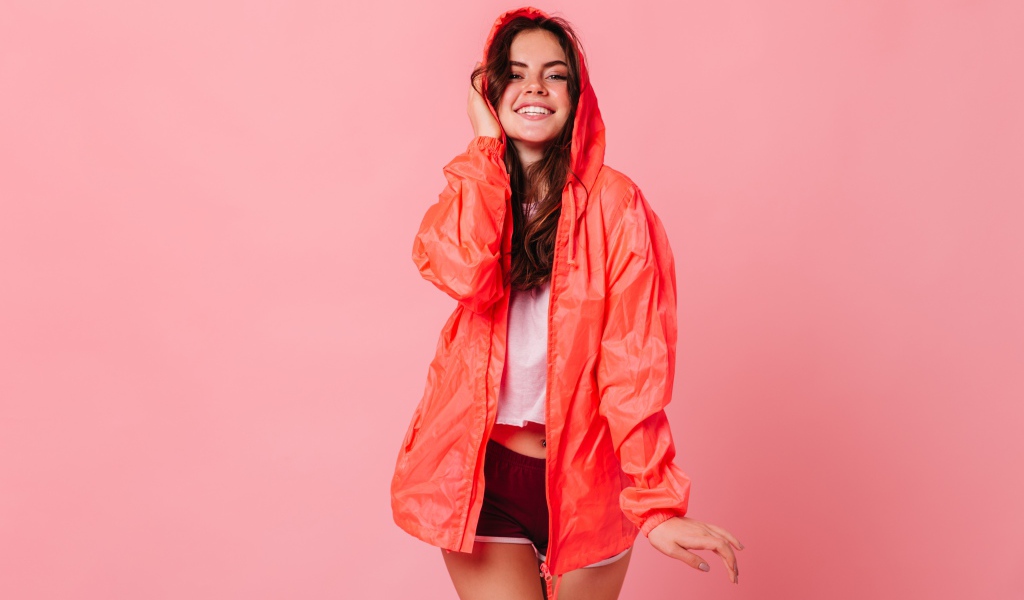 Улыбающаяся девушка в плаще на розовом фоне