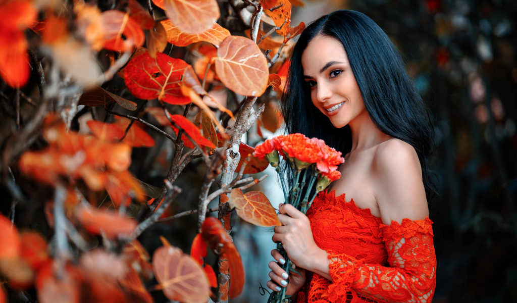 Улыбающаяся девушка с букетом гвоздик у стены с осенними листьями