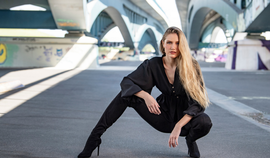 Стильная девушка в черном костюме под мостом