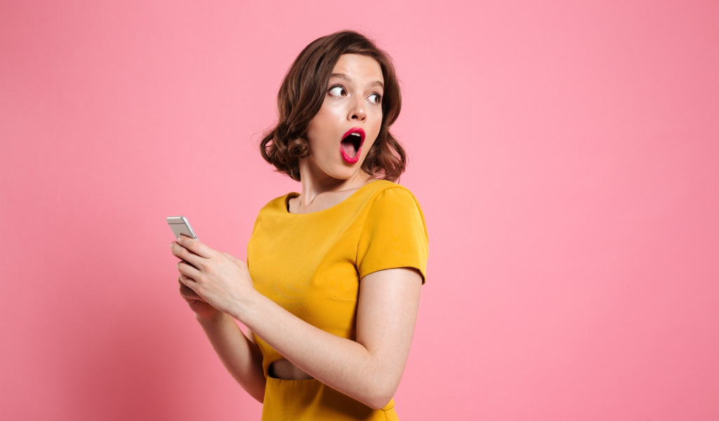 Удивленная девушка с телефоном в руках на розовом фоне