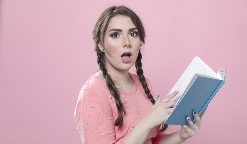 Удивленная девушка с книгой на розовом фоне