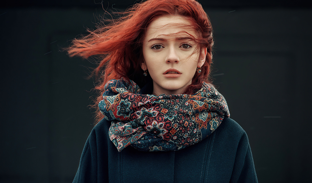 Ветер развивает волосы рыжеволосой девушки в пальто