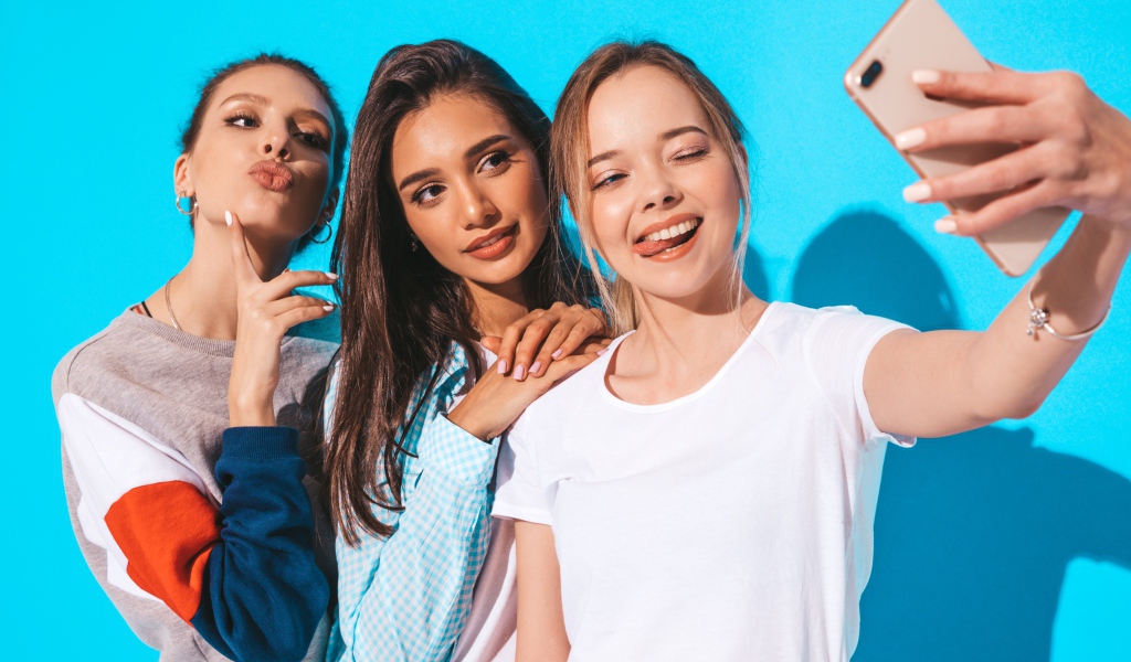 Три подруги делают селфи на голубом фоне