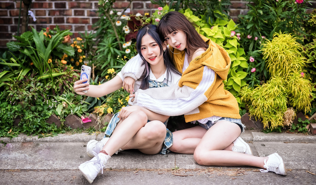 Две девушки азиатки сидят у стены с цветами 