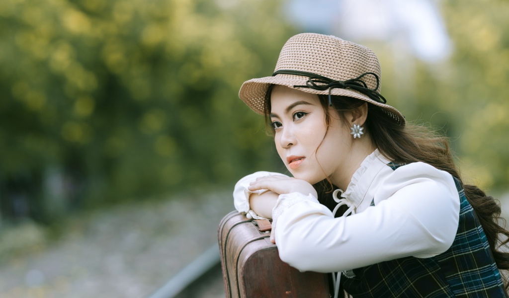 Молодая азиатка в шляпе с чемоданом