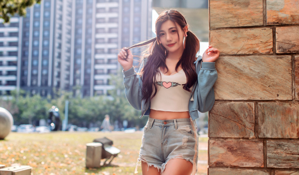 Молодая азиатка в коротких шортах стоит у стены