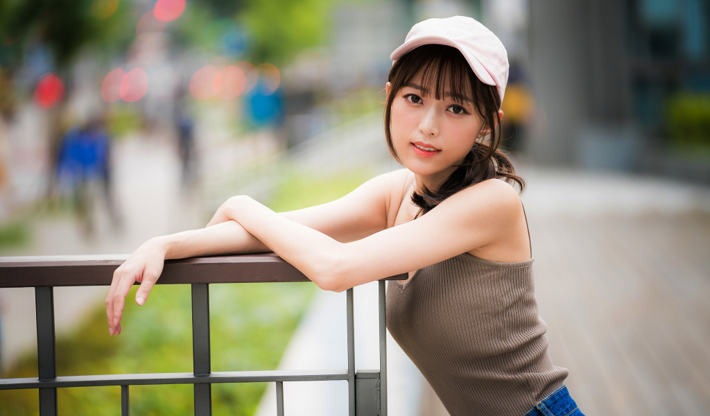 Молодая азиатка в кепке у перил 