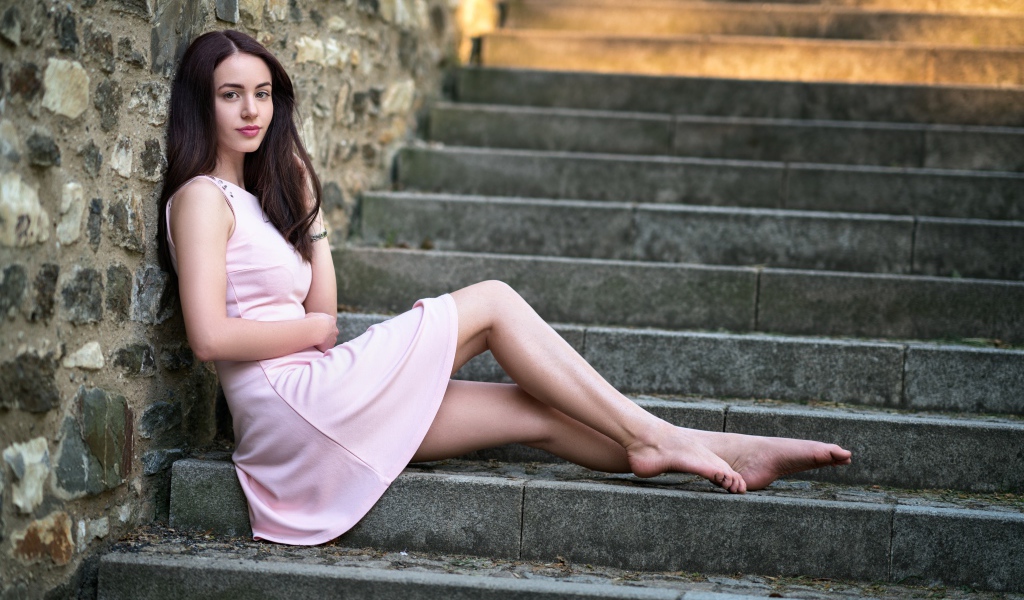 Молодая девушка в розовом платье на ступеньках у стены 