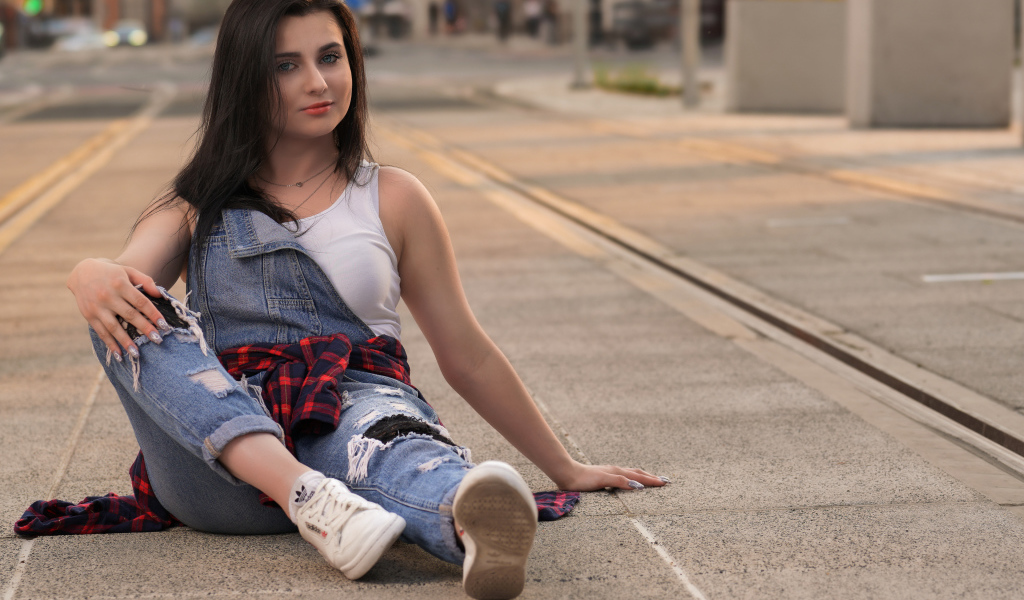 Молодая девушка в джинсовом наряде сидит на асфальте