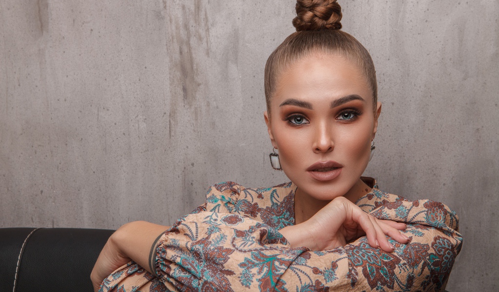 Молодая девушка с прической на голове на фоне стены