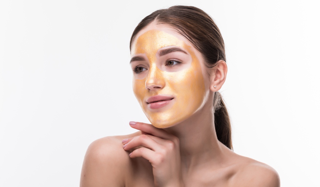 Молодая девушка без макияжа с золотой маской на лице