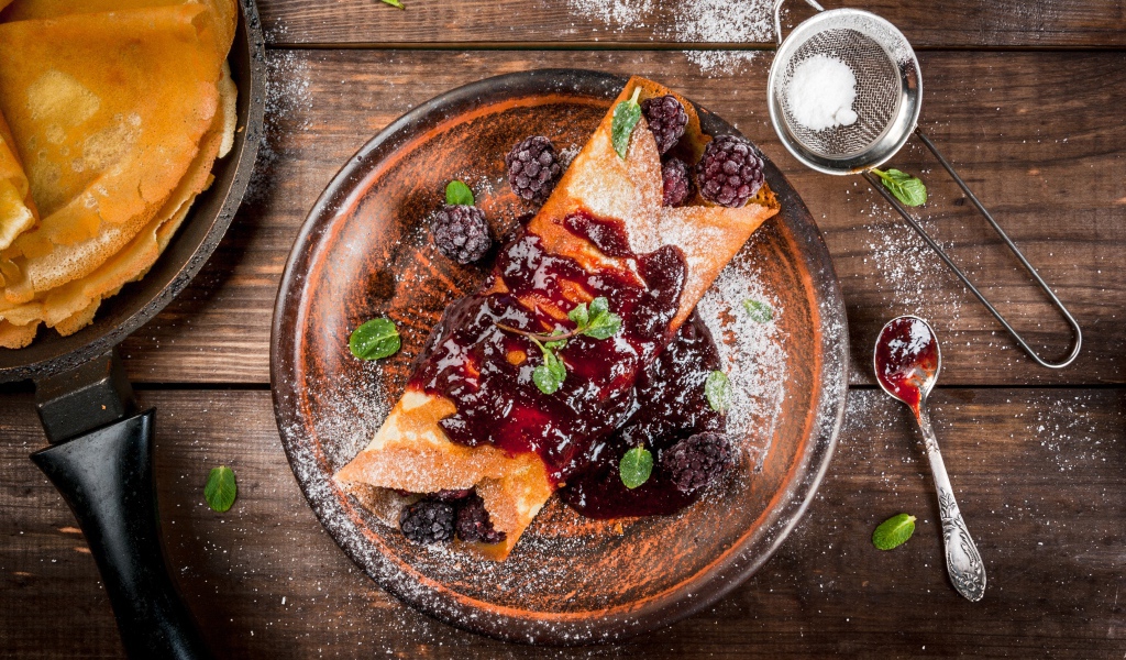 Блин с ягодами и джемом на тарелке с сахарной пудрой