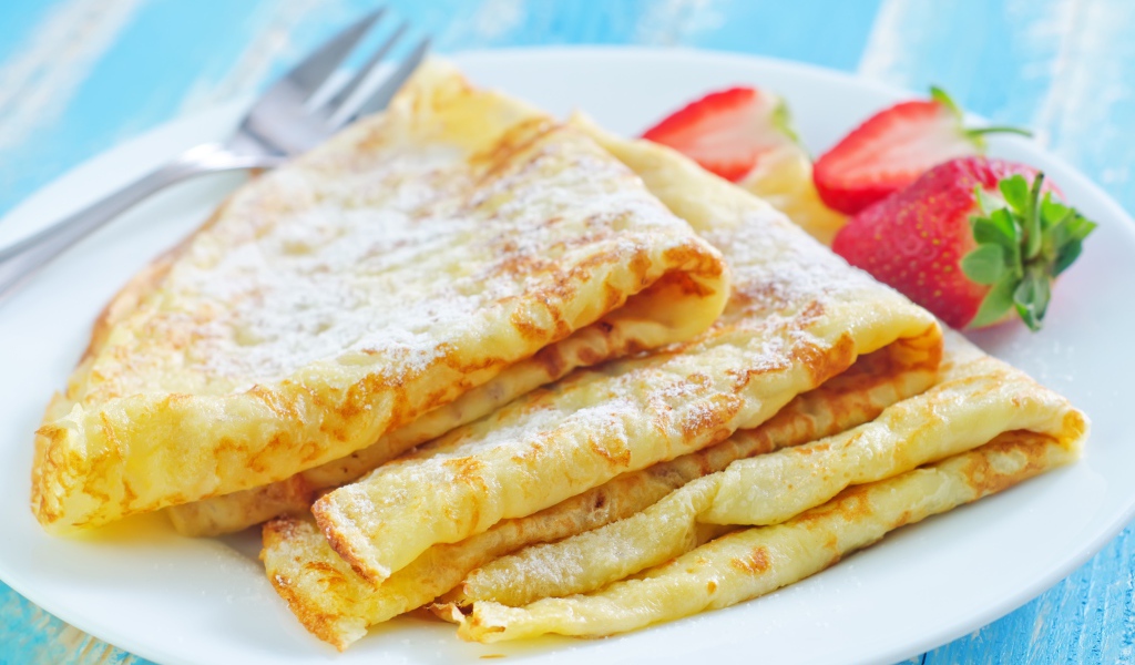 Румяные тонкие блинчики на тарелке с клубникой 