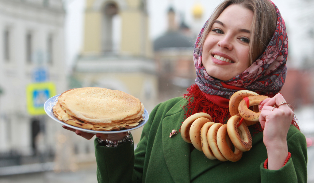 Улыбающаяся девушка с блинами и баранками на Масленицу
