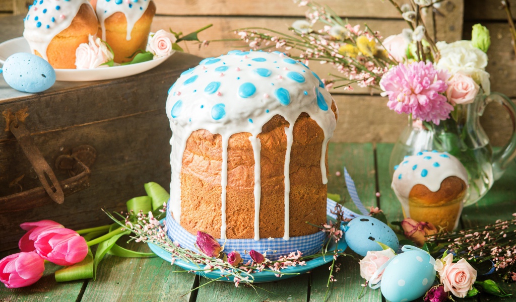 Красивый пасхальный кулич с белой глазурью на столе с цветами