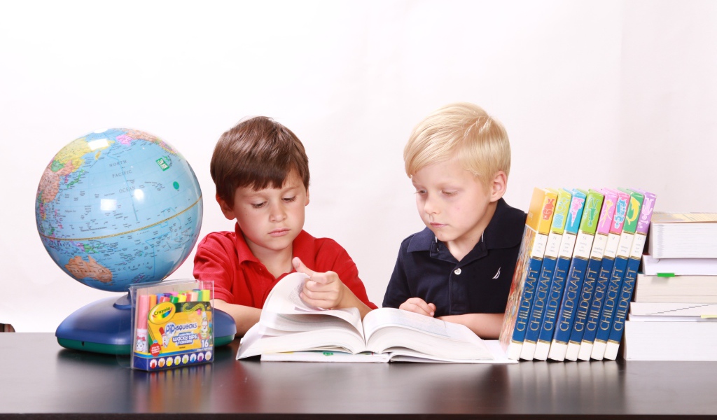 Два мальчика школьника с книгами и глобусом за столом