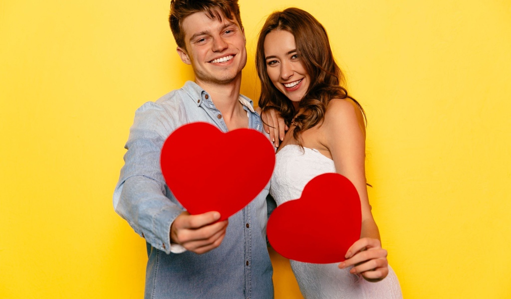 Влюбленная пара на желтом фоне с бумажными сердечками в руках 