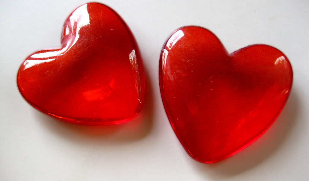 Два красных стеклянных сердца на сером фоне