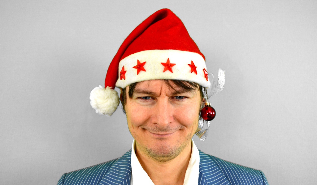 Голубоглазый мужчина в новогодней шапке на сером фоне 