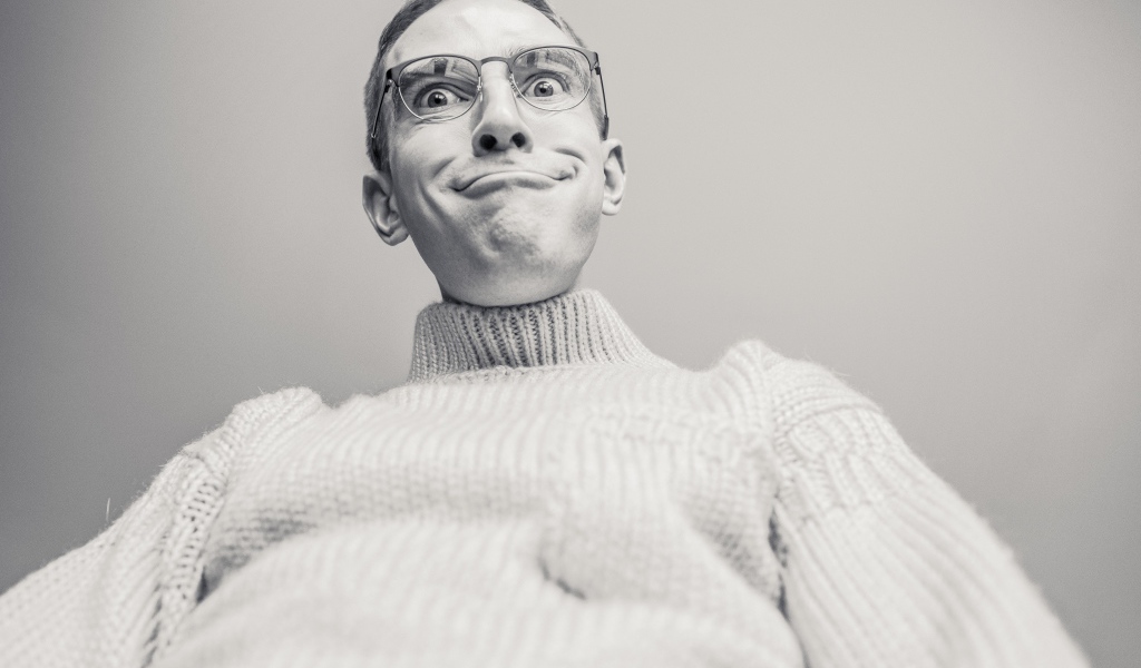 Мужчина в очках корчит лицо на сером фоне