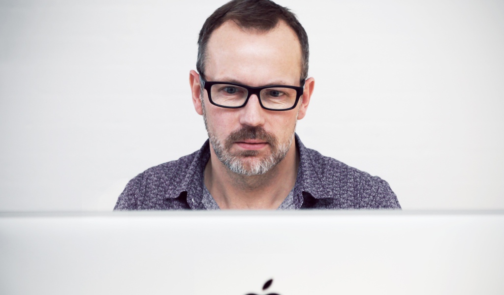 Серьезный мужчина в очках сидит за макбуком