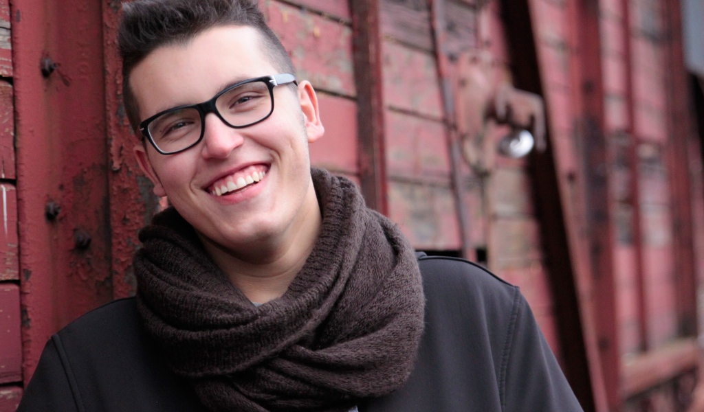 Улыбающийся мужчина в очках у стены 