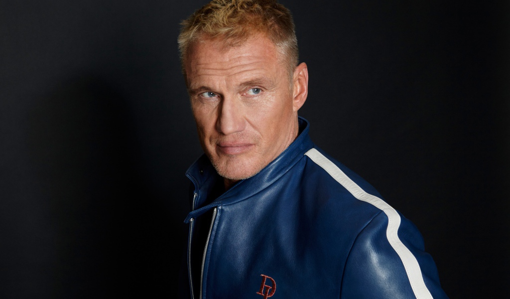 Актер Дольф Лундгрен в куртке на фоне  серой стены