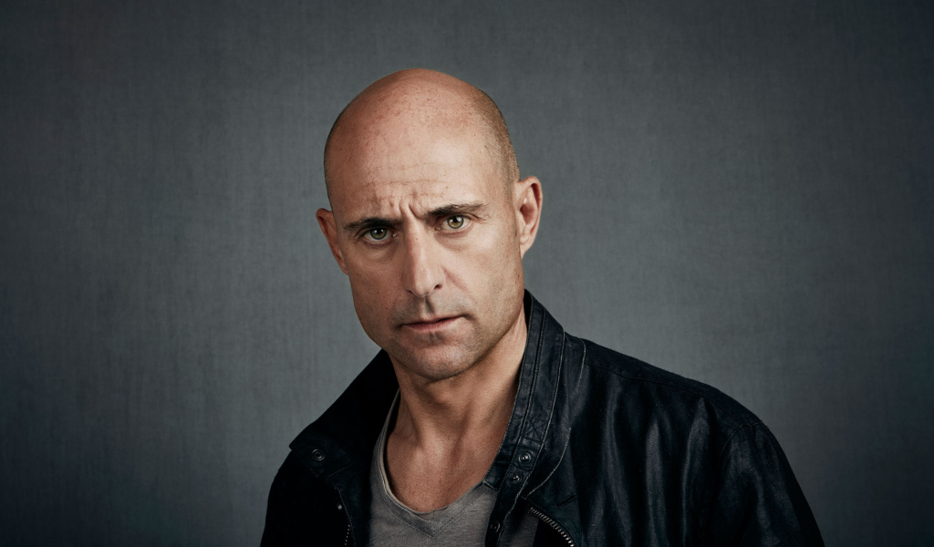 Марк Стронг в черной куртке на сером фоне