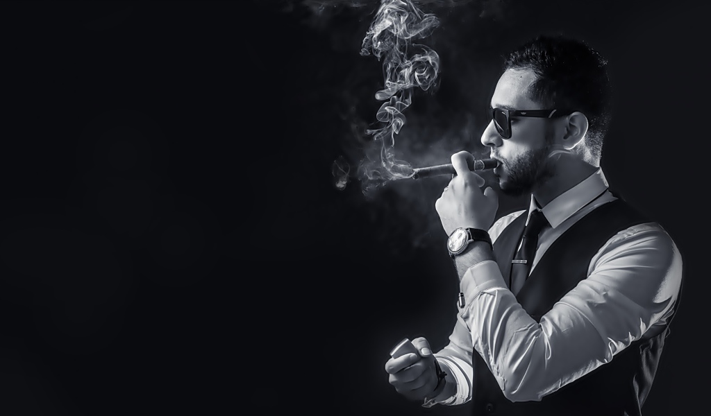 Мужчина с сигарой в руке на черном фоне 