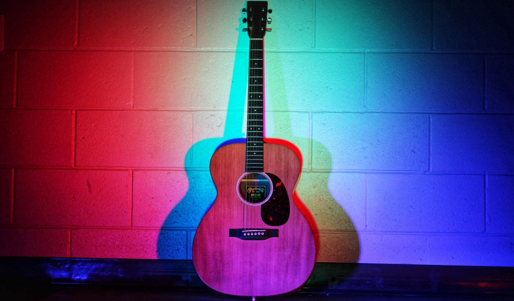 The guitar stands against the wall in a multicolored light