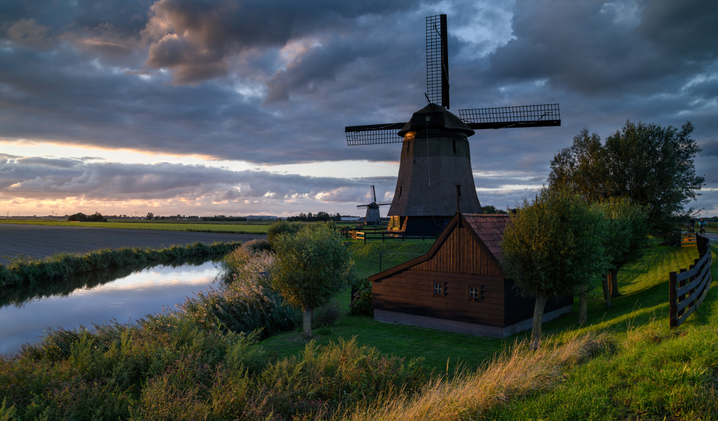 Большая ветряная мельница у реки на закате