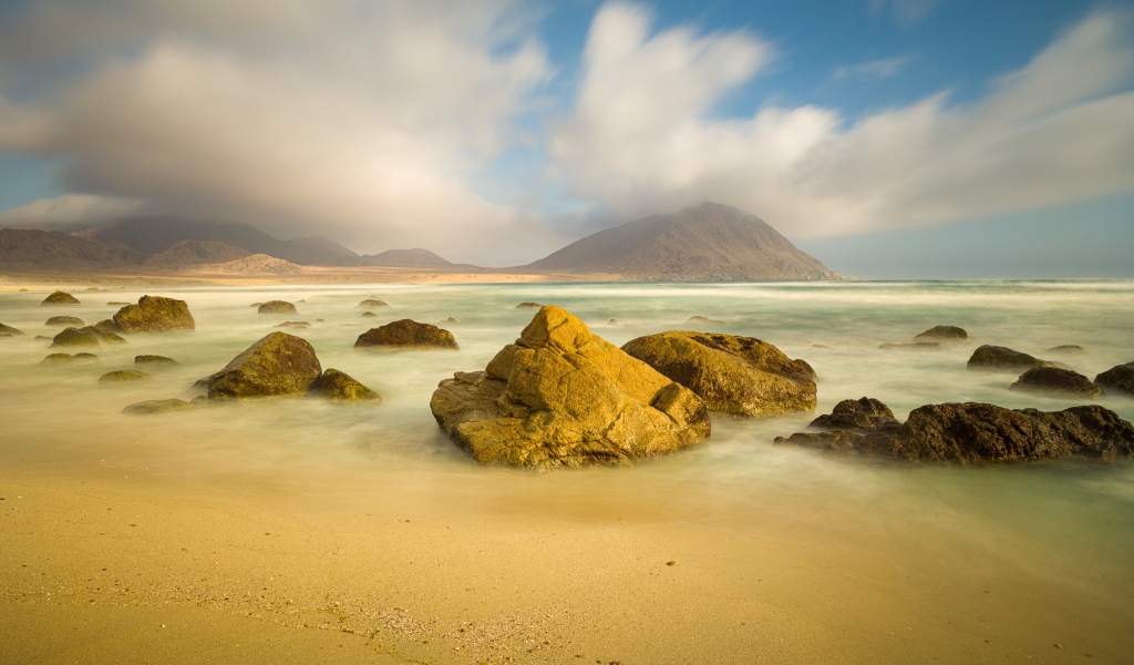 Большие камни лежат в воде на песке 