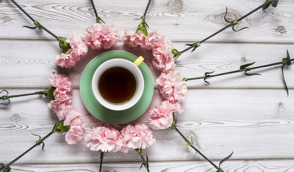Розовые гвоздики с чашкой чая на деревянном столе 