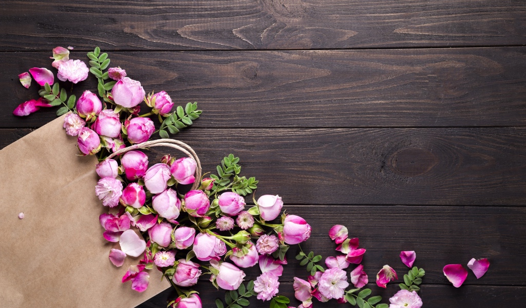 Цветки розовой розы с бумажным пакетом  на деревянном фоне