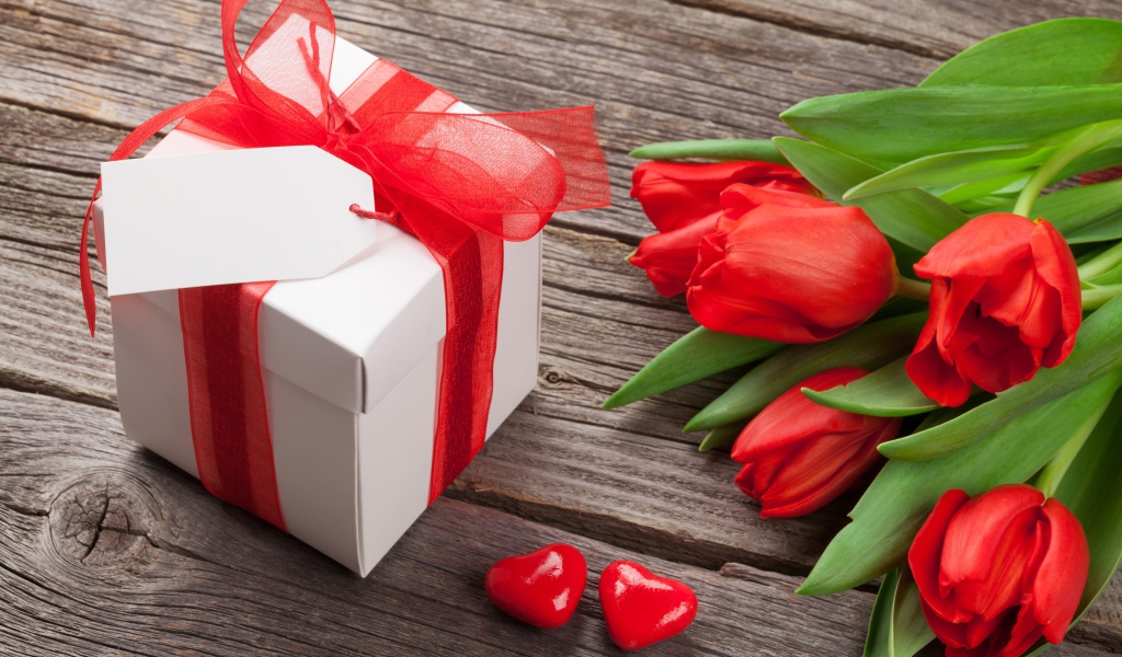 Красные тюльпаны с большим подарком на деревянном столе 