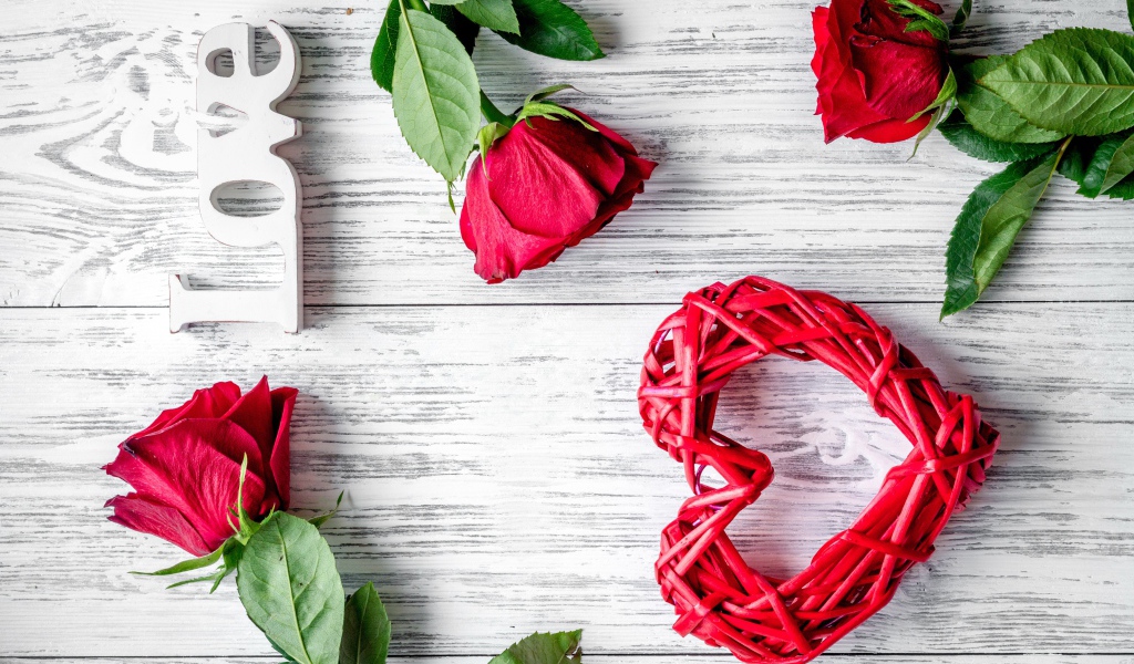 Красное плетеное сердце с алыми розами на деревянном столе