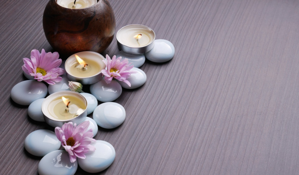 Камни с хризантемами и зажженными свечами на столе 